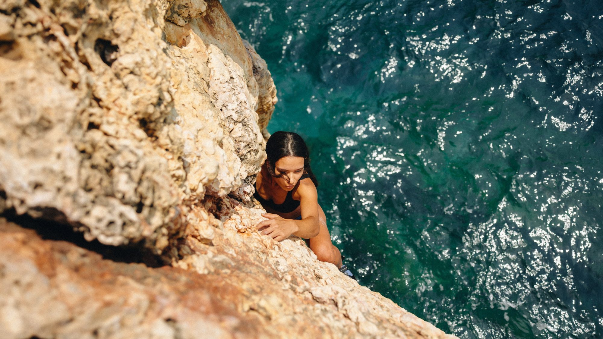 Climber on a sea cliff above turquoise water, deep water solo